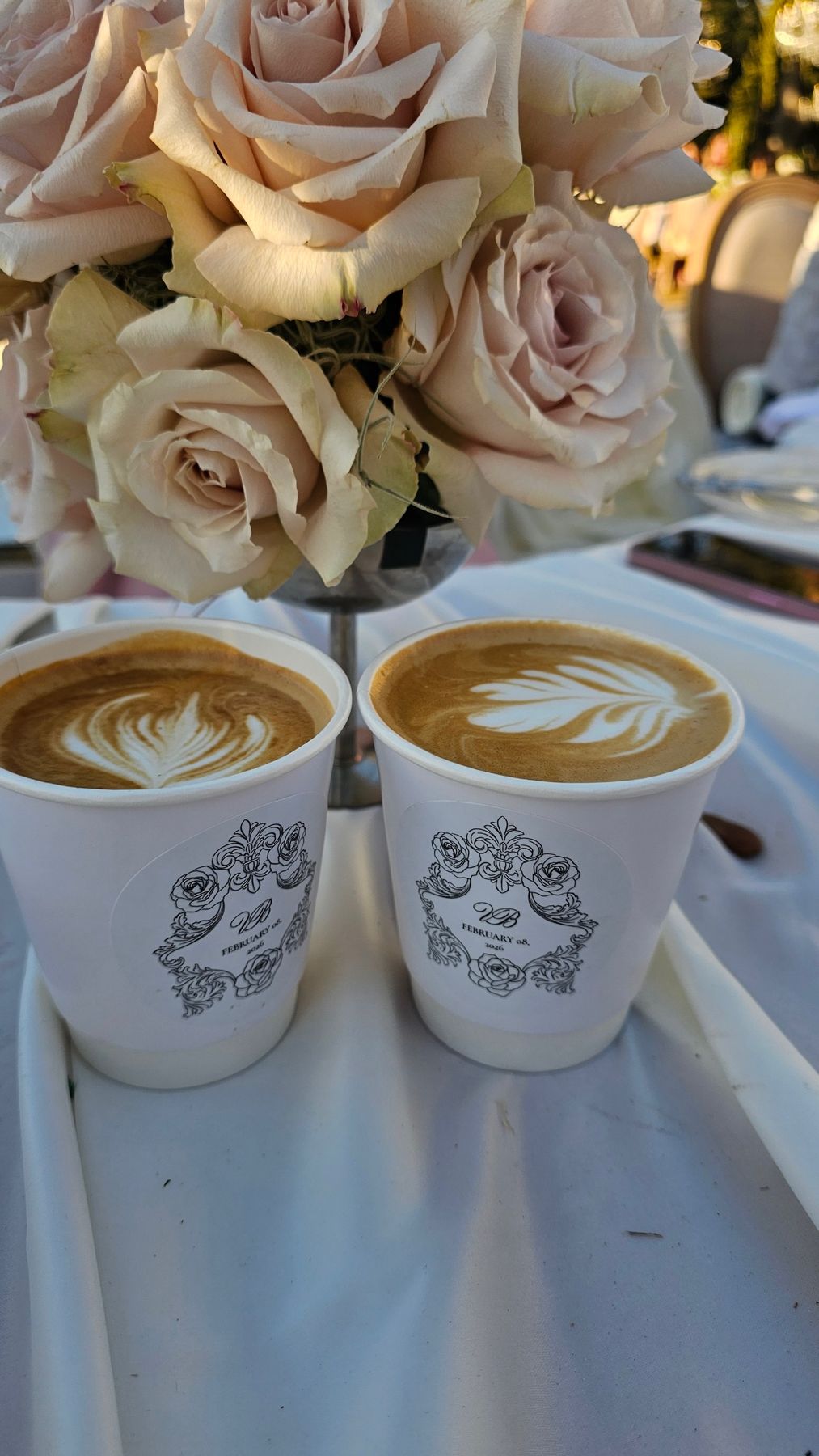 Two lattes with latte art next to blush roses