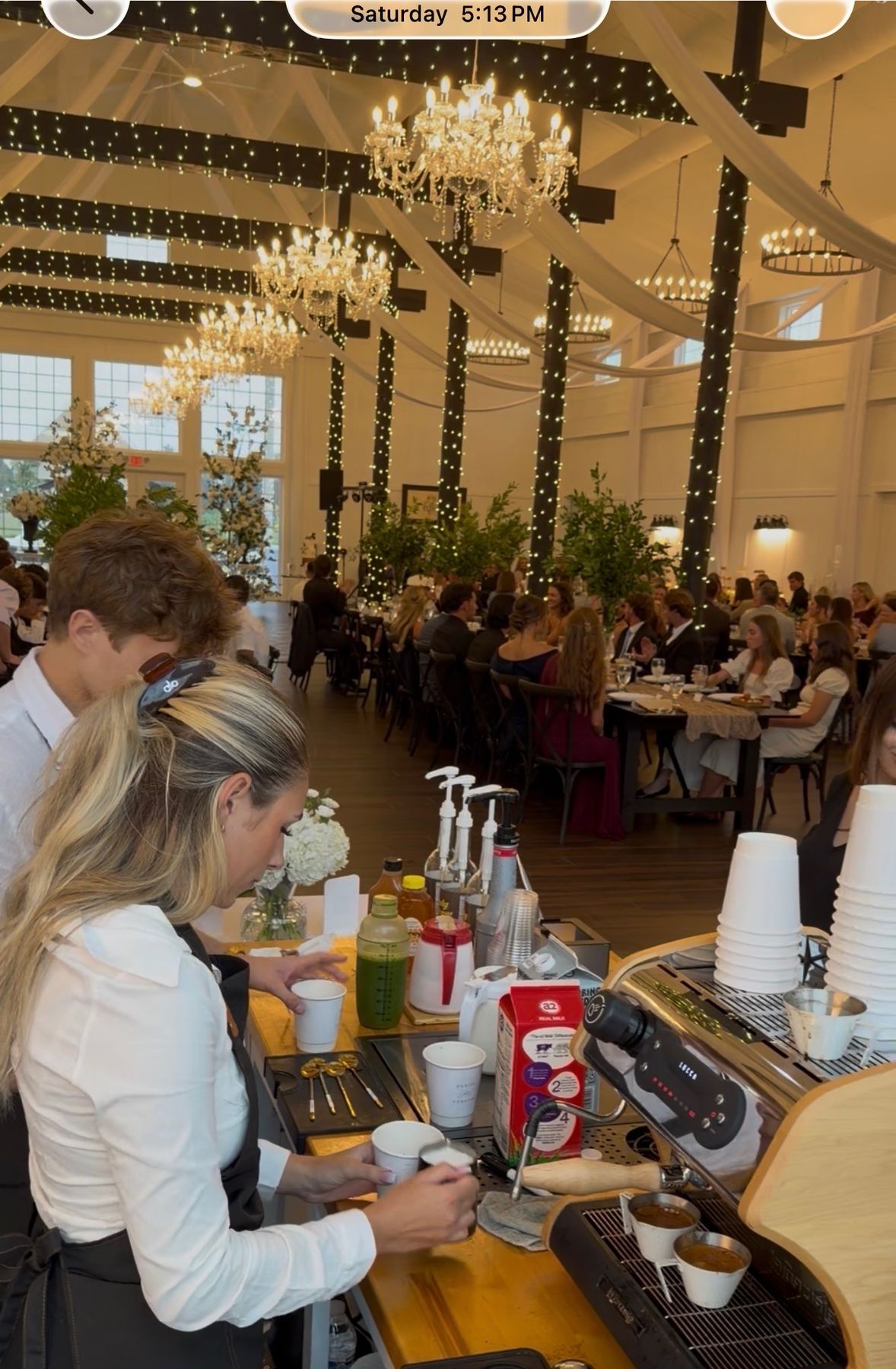 Barista making coffee at a wedding reception under chandeliers